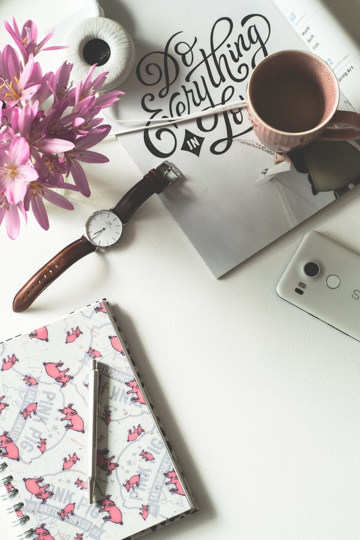 Top view of a chic feminine workspace featuring coffee, flowers, and stationery.